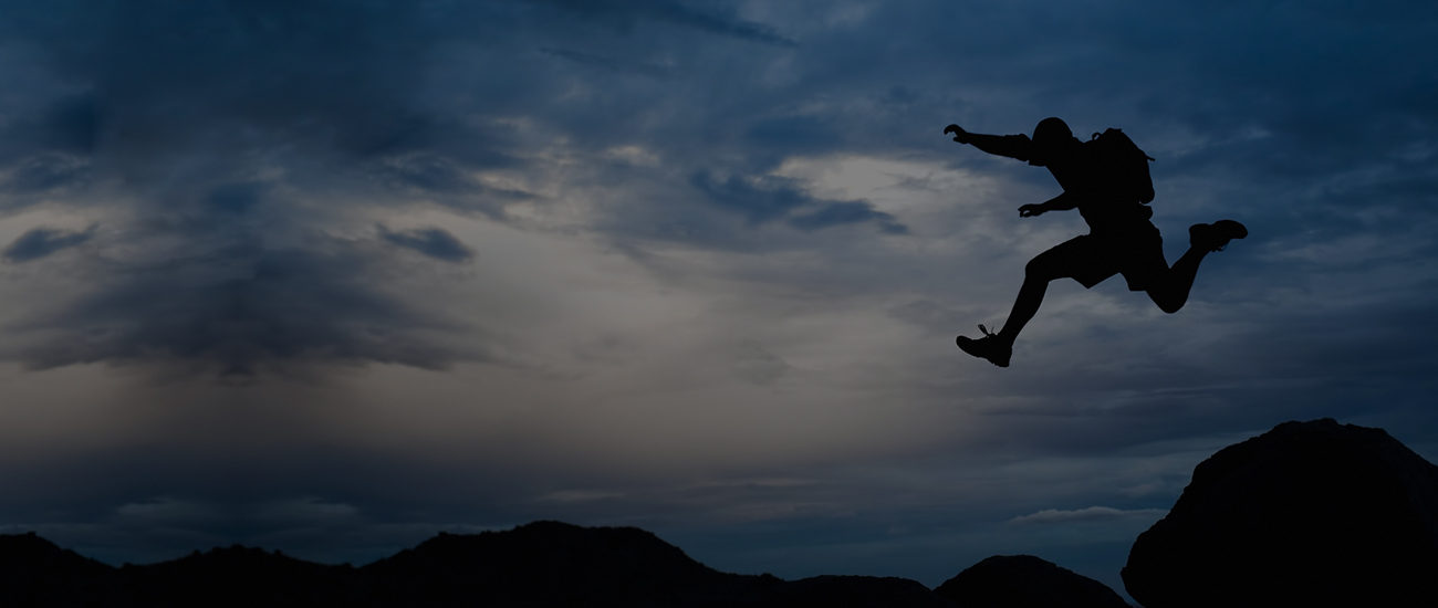 Silhouette of a person jumping between rocks against a twilight sky.