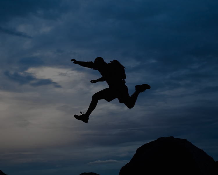Silhouette of a person jumping between rocks against a twilight sky.