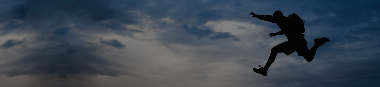 Silhouette of a person jumping between rocks against a twilight sky.